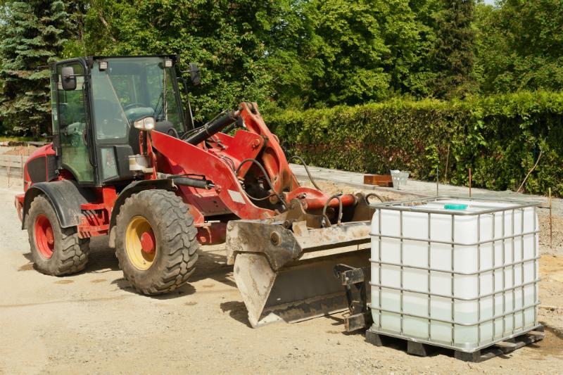 Ein roter Radlader steht neben einem Tank fuer Bauwasser