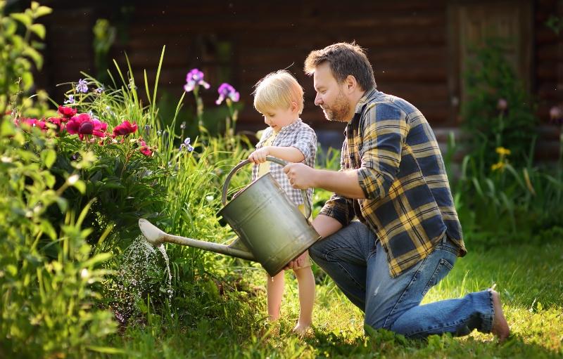 Mann gießt seinen Garten, nebendran ein kleines Kind