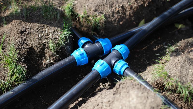 In einem Graben werden Wasserleitungen in einem Garten verlegt. 
