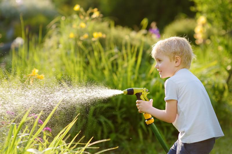 Junge versprüht Wasser mit Gartenschlauch, beispielsweise mittels IBC Container mit Schlauchanschluss 