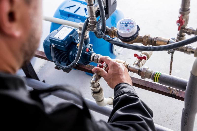 Ein Mann überprüft die Rohre und Zuflüsse eines Hauswasserwerks Hauswasserwerk oder Hauswasserautomat