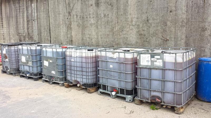 Mehrere, mit einer braunen Flüssigkeit gefüllte IBC-Container stehen nebeneinander vor einer Betonwand IBC Container Abwasser