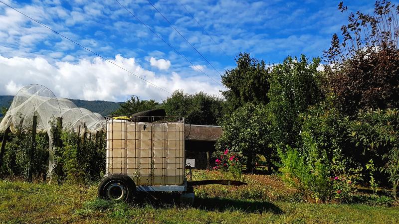 Vor einem blühenden Garten ist ein IBC-Container auf einem zweiachsigen Wagen platziert