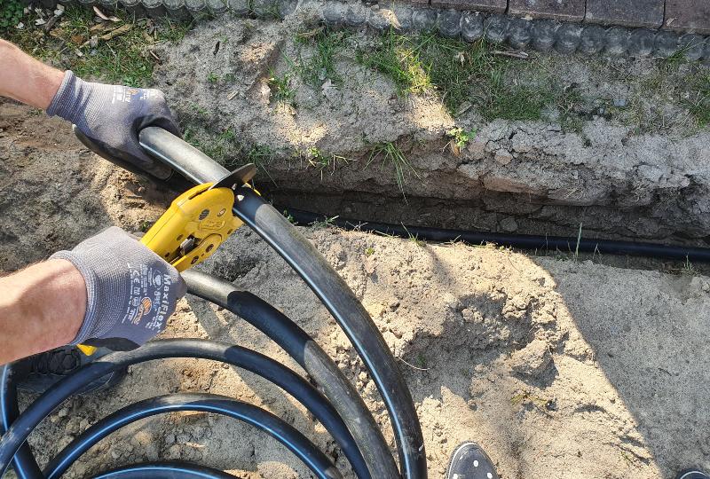 Arbeiten an einer unterirdischen Gartenbewässerung, jemand schneidet ein PE-Rohr in die passende Länge