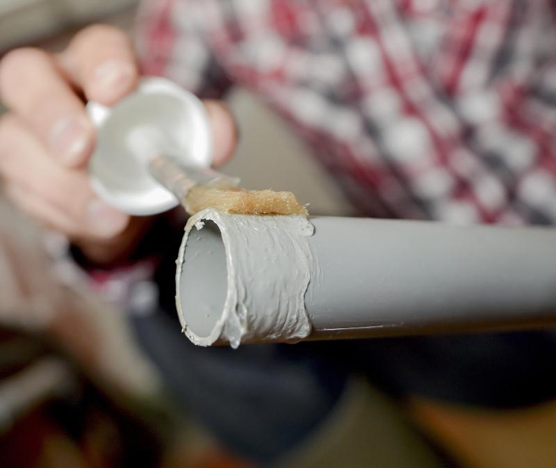 Jemand bestreicht das Ende eines PVC-Rohrs mit Klebstoff PVC Rohre verkleben