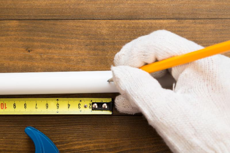 Jemand zeichnet mit einem Stift ein PVC-Rohr an der Stelle an, an der er es absägen möchte PVC Rohre verkleben