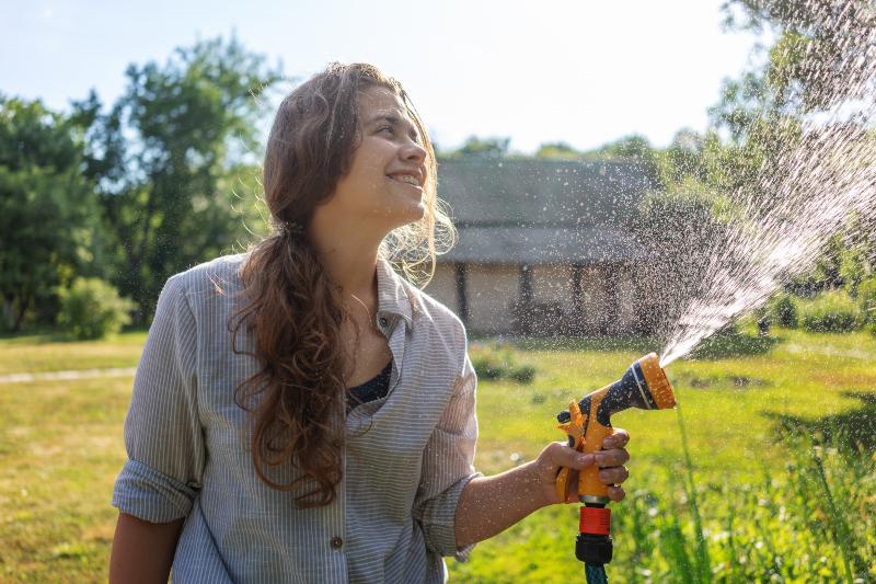 Eine junge Frau gießt den Garten mit einem Schlauch