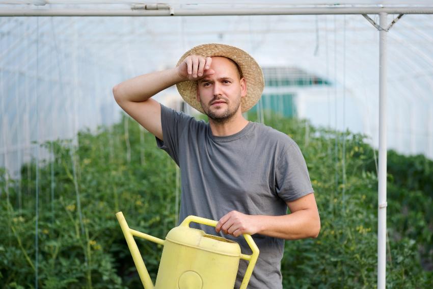 Mann mit Gießkanne wischt sich die Stirn - Automatische Pflanzenbewässerung ist angenehmer