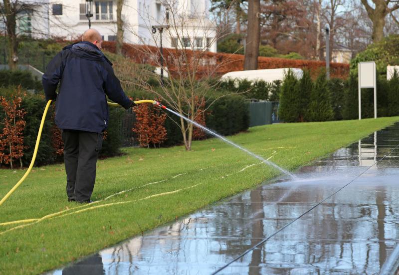 Ein Mann reinigt mit einem Wasserschlauch einen Gartenweg Wasseranschlussdose