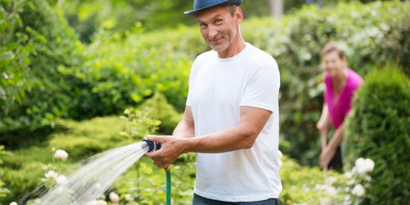 Mann mit Gartenschlauch gießt Blumen