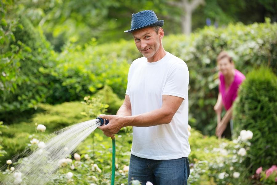 Mann mit Gartenschlauch gießt Blumen