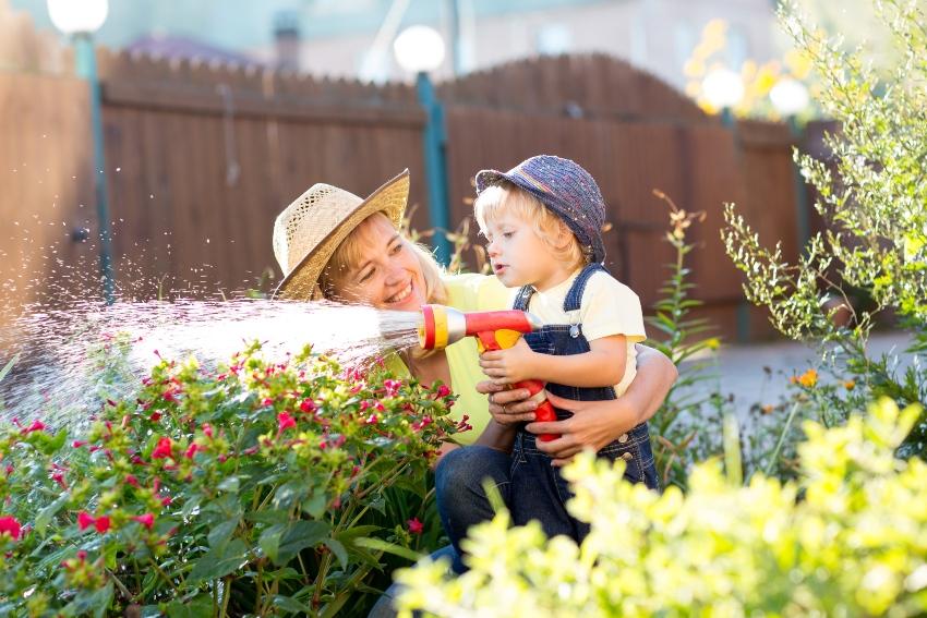 Kind gießt Blumen mit Gartenschlauch