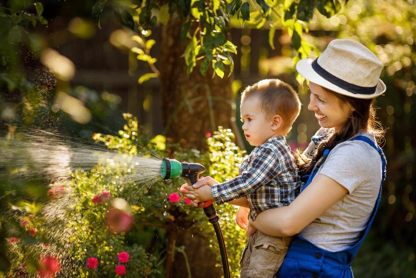 Mutter mit kleinem Kind bei der Gartenbewässerung