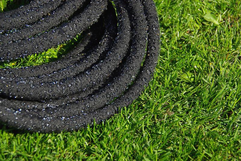 Ein Perlschlauch liegt auf einer Rasenfläche, durch die feinen Poren treten Wassertropfen aus