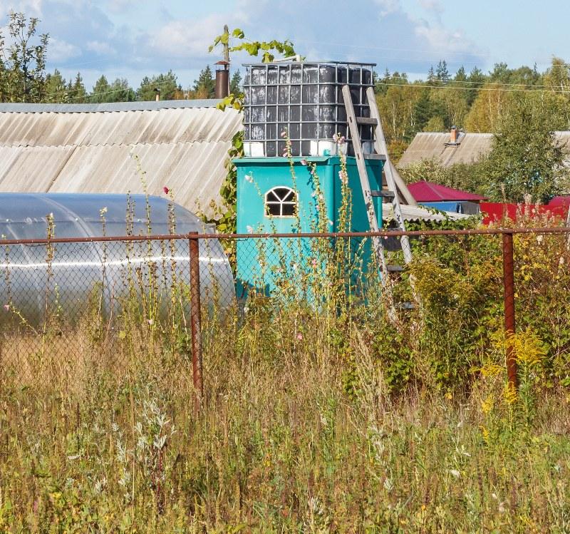 Auf dem Dach der Duschkabine einer selbstgebauten Gartendusche ist ein IBC-Container positioniert