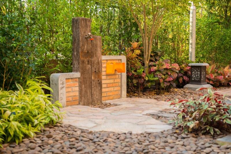 Eine kunstvoll gestaltete Außenzapfstelle im Garten, die Leitung verläuft in einer großen Holzbohle und die gesamte Anlage ist in eine kleine Mauer eingelassen