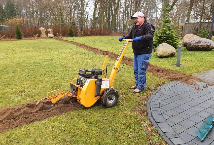 Jemand nutzt Maschine, um Gräben für Wasserleitungen im Garten anzulegen - Versenkbare Gartenbewässerung planen