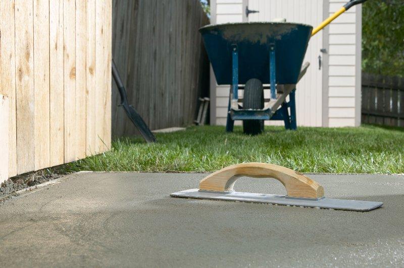 Ein frisch gelegtes Betonfundament im Garten härtet aus. Im Hintergrund steht eine Schubkarre Fundament 