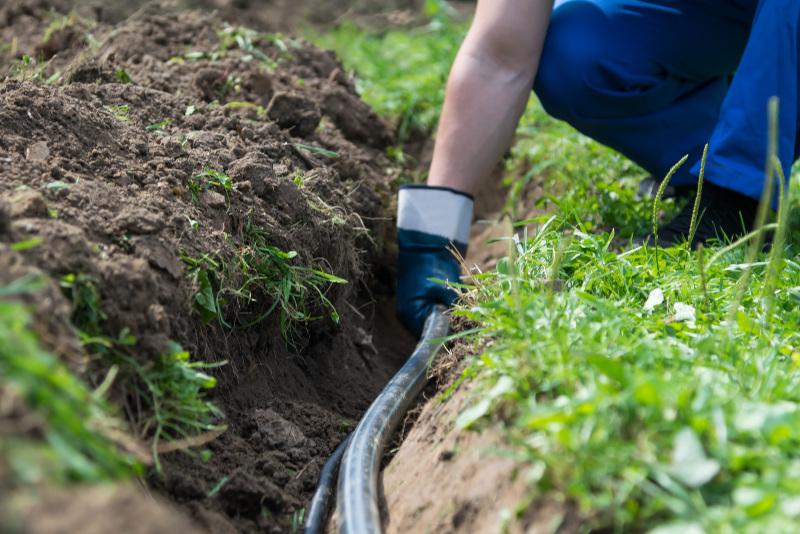 Ein Mann verlegt ein PE-Rohr in einem Graben im Garten