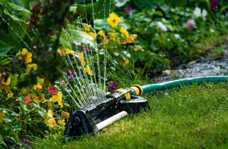 Ein Viereckregner bewässert ein Blumenbeet große Flächen