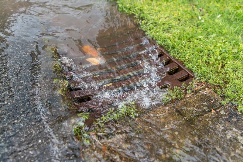 Regenwasser fließt in den Deckel der Kanalisation Niederschlagswassergebühr