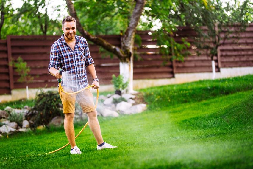 Mann bewässert seinen Rasen mit einem Gartenschlauch - er verzichtet auf Automatische Gartenberegnung