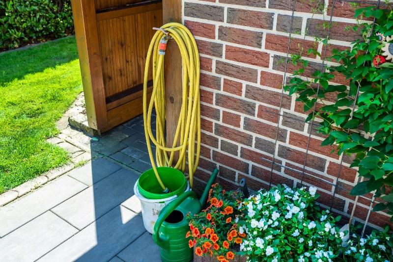 Vor einem Außenwasserhahn in einem sommerlichen Garten stehen Eimer und Gießkanne bereit Wasserdruck verstärken