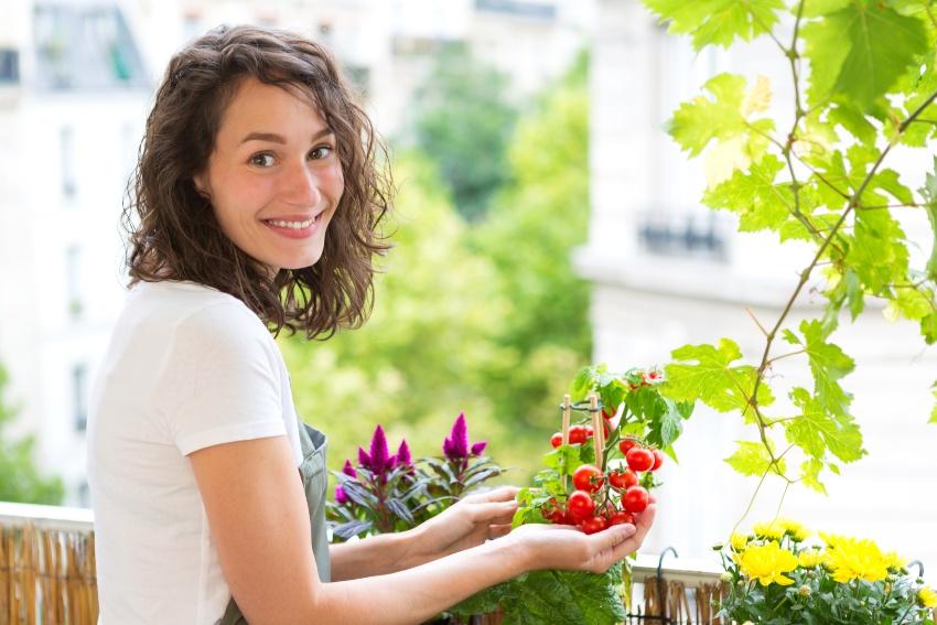 Junge Frau auf dem Balkon mit ihren Pflanzen - Balkonblumen gießen