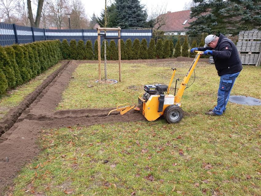 Jemand hebt mit einer Maschine Gräben aus für die Gartenbewässerung - Vollautomatische Rasensprinkleranlage