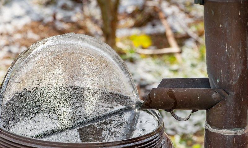 Auf einer Wassertonne, die unter einem Fallrohr platziert ist, hat sich Eis gebildet