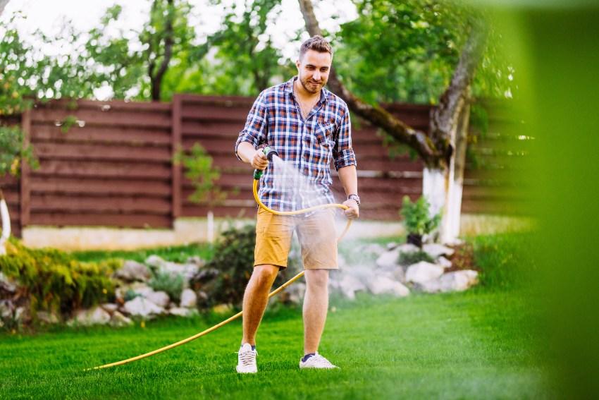 Mann bewässert seinen Rasen mit Gartenschlauch - Beim Gartenwasser Geld sparen?