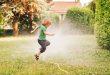 Kind springt über Gartenschlauch - Schlauchregner für Grünflächen