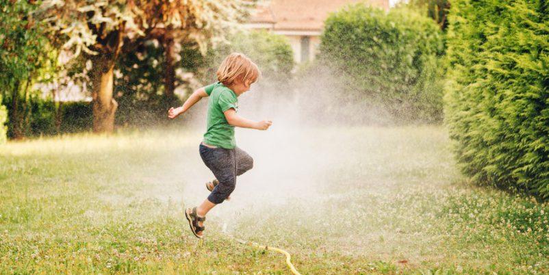 Kind springt über Gartenschlauch - Schlauchregner für Grünflächen