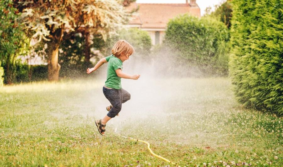 Kind springt über Gartenschlauch - Schlauchregner für Grünflächen