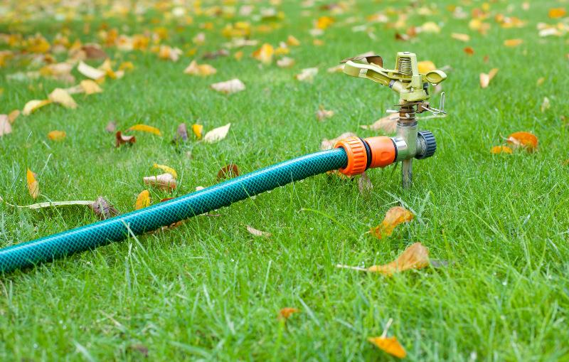 Auf einem Rasen mit Herbstlaub wartet ein Rasensprenger auf den Einsatz