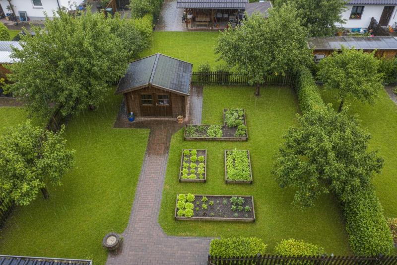 Schrebergarten mit Gartenhaus, Hochbeeten und Apfelbäumen aus der Vogelperspektive im Regen
